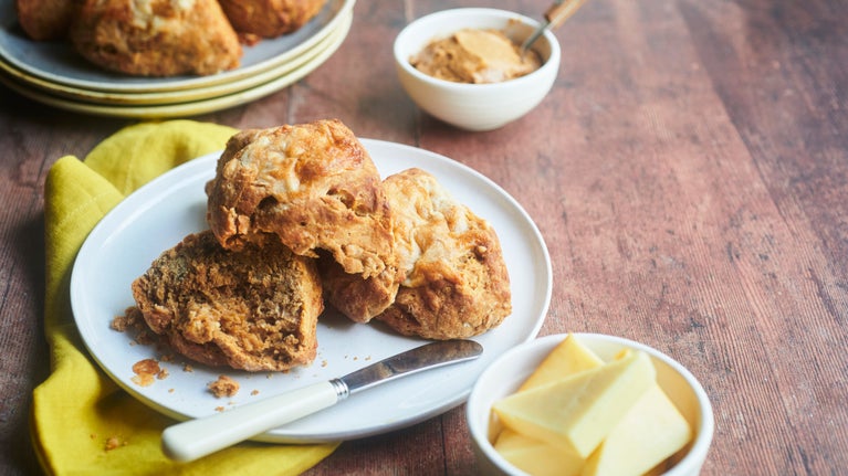 Scones are piled on a plate with a knife and some butter.